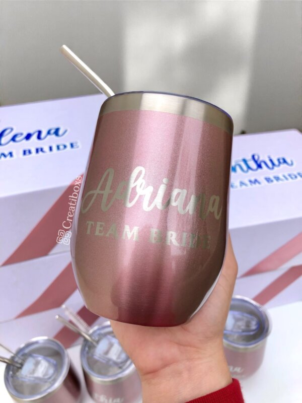 Una mano sostiene un vaso metálico rosa con la etiqueta "Adriana TEAM BRIDE" con una pajita. Termos personalizados para boda, perfectos para celebraciones de despedida de soltera y regalos de boda únicos.