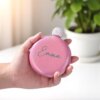 Una mano sostiene una Licorera personalizada de acero inoxidable 148ml 5oz rosa y redonda con la etiqueta Emma junto a una maceta verde.