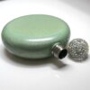 Sobre una superficie blanca descansa una reluciente Licorera personalizada de acero inoxidable 148ml 5oz de color verde menta con un brillante tapón enjoyado.
