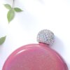 Licorera redonda, rosa brillante personalizada de acero inoxidable 148ml 5oz con tapón joya, colocada junto a hojas verdes sobre fondo blanco.