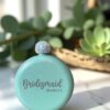 La Licorera personalizada de acero inoxidable 148ml 5oz con tapa brillante etiquetada "Bridesmaid Isabella" se encuentra entre plantas, un encantador regalo personalizado o recuerdo.