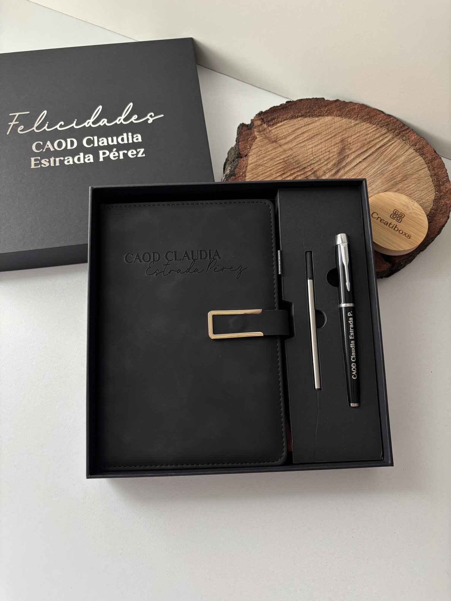 Caja de regalo con un Set libreta con broche magnético contorno metálico y bolígrafo en caja, etiquetado personalizado CAOD Claudia Estrada Pérez en la portada, además de un elegante bolígrafo y lápiz.