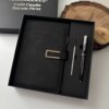 Caja de regalo negra con un Set libreta con broche magnético contorno metálico y bolígrafo en caja, además de un lápiz y un posavasos de madera sobre una superficie blanca.