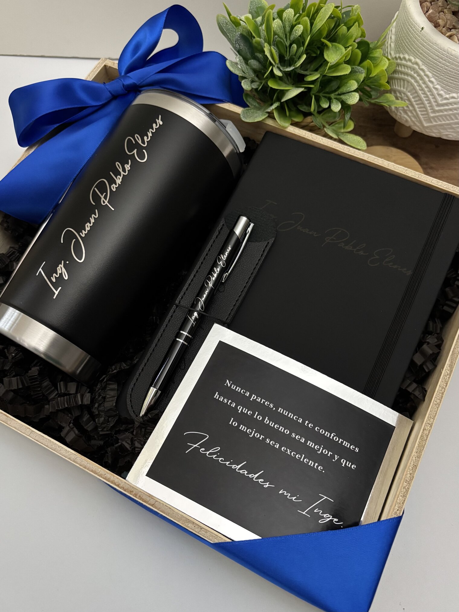 Kit regalo corporativo incluye termo clásico 590 ml, libreta y bolígrafo personalizados con tarjeta, presentado con listón azul junto a planta.
