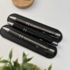 Dos bolígrafos metálicos personalizados con acabado brillante y detalles plateados, cada uno grabado con nombres, colocados en un estuche negro junto a una caja de madera Creartiboxs.