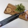 Una mano sostiene un bolígrafo personalizado metálico con acabado brillante y detalles plateados en una funda, con una planta y una tabla de madera al fondo.
