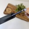 Una mano tira de un bolígrafo personalizado mate con acabado soft touch y detalles plateados, rotulado LIC. BRENDA MEDINA, de un estuche negro junto a una planta y una tabla de madera.