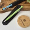 Dos bolígrafos mate personalizados con acabado soft touch y detalles plateados, en estuches, descansan sobre un tablero de madera -uno verde etiquetado Samantha Morales- cerca de una tapa redonda Creatiboxs.