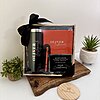 Kit regalo corporativo con termo delgado 590ml, libreta y bolígrafo personalizado con tarjeta, sobre una tabla de madera rodeada de plantas.