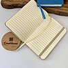 Una mini libreta en blanco personalizada abierta con elástico y una cinta amarilla, una mini libreta azul cerrada y un posavasos de madera Creatiboxs.