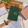 Una Agenda organigastos personalizada A6 con cierre magnético metálico, más separadores etiquetados en una bandeja de madera junto a una pequeña planta.