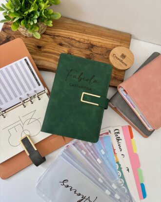 Una Agenda organigastos personalizada A6 con cierre magnético metálico, más separadores etiquetados en una bandeja de madera junto a una pequeña planta.