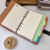 Agenda personalizada A6 "Agenda planner organigastos" con cierre magnético metálico, calendario y páginas rayadas, separadores de pestañas de colores, más un posavasos Greatibox de madera.