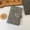 Agenda personalizada organigastos A6 con cierre magnético metálico, cubierta de piel gris con el nombre de Amelia Pérez, expuesta sobre una superficie de madera.
