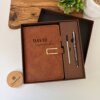 Set libreta con broche magnético contorno metálico y bolígrafo en elegante caja de regalo; fondo decorado con plantas.