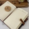 El Set libreta con broche magnético contorno metálico y bolígrafo en caja está colocado sobre un escritorio junto con un posavasos de madera Creatiboxs y una maceta.