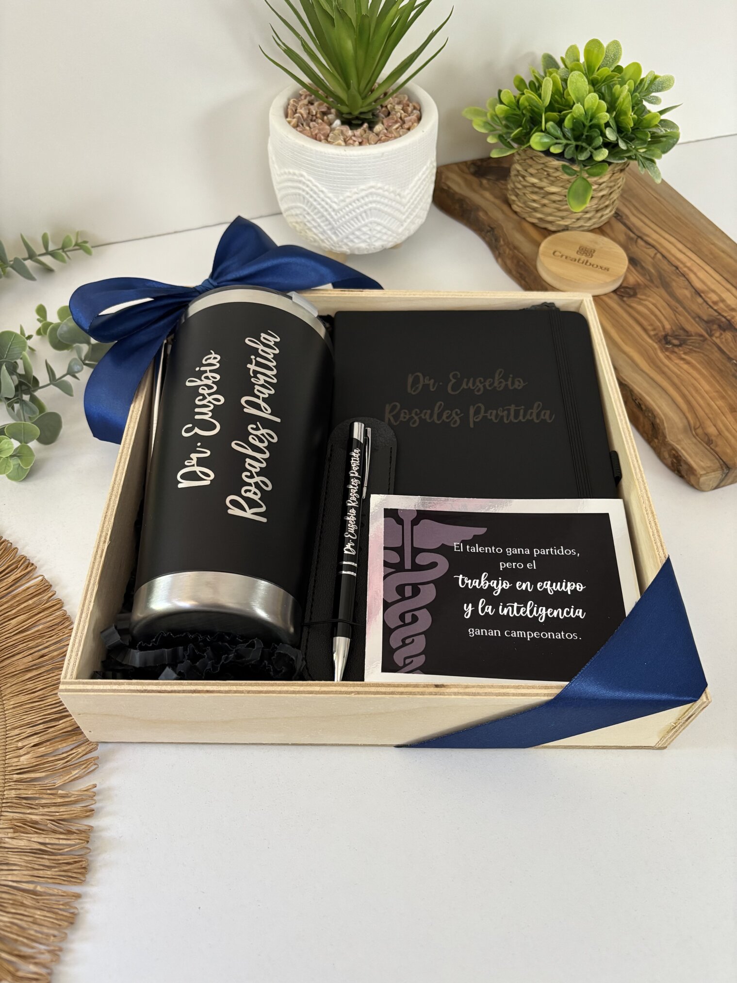 Kit regalo corporativo con termo clásico 590ml, libreta y bolígrafo personalizados y tarjeta, todo etiquetado Dr. Eusebio Rosales Partilla junto a una planta. Ideal para un obsequio empresarial especial.