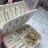 Un joyero personalizado de cuero sintético chico exhibe anillos, aretes y collares dorados sobre una encimera de mármol.