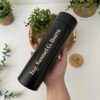 Una mano sostiene un Termo personalizado digital liso 500ml 16oz con la inscripción "Ing. Samuel G. Ibarra". Samuel G. Ibarra", rodeado de plantas.