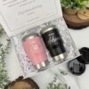 Kit termo portalatas x2 y caja personalizada chica magnética: Incluye dos vasos personalizados, uno rosa con "Madrina Katia" y otro negro con "Padrino Adrián", presentados entre plantas en una elegante caja magnética.