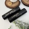 Dos vasos negros Termo personalizado digital liso de 500 ml con los nombres de Anna Luisa García y Carlos Gómez en letra de imprenta blanca, sobre una superficie blanca.