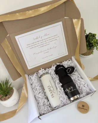 La caja de regalo incluye un "Kit porta botellas + termo delgado 590ml y caja personalizada md" personalizado, una nota, una cinta y pequeñas plantas decorativas cerca.