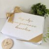 Caja de regalo blanca con cinta dorada, texto en letra dorada y decoración vegetal verde, ideal como caja personalizada para padrinos