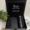Kit regalo personalizado en caja negra con termo delgado 590ml, libreta vertical con cierre magnético y bolígrafo, todos con nombre en grabado laser, elegantemente presentados junto a una planta en maceta.