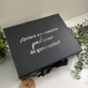 Caja de regalo personalizada color negro con texto en español, ¿Quiere ser nuestro padrino de generación?, sobre una superficie blanca con plantas. Este kit regalo personalizado incluye un termo delgado de 590ml, libreta cierre magnético, y bolígrafo. Perfecto para padrinos