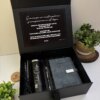 Kit regalo personalizado en caja negra con termo delgado 590ml, libreta broche metálico y bolígrafo, ideal para cualquier ocasión. Incluye nota de agradecimiento y se presenta rodeado de plantas verdes para un toque elegante.
