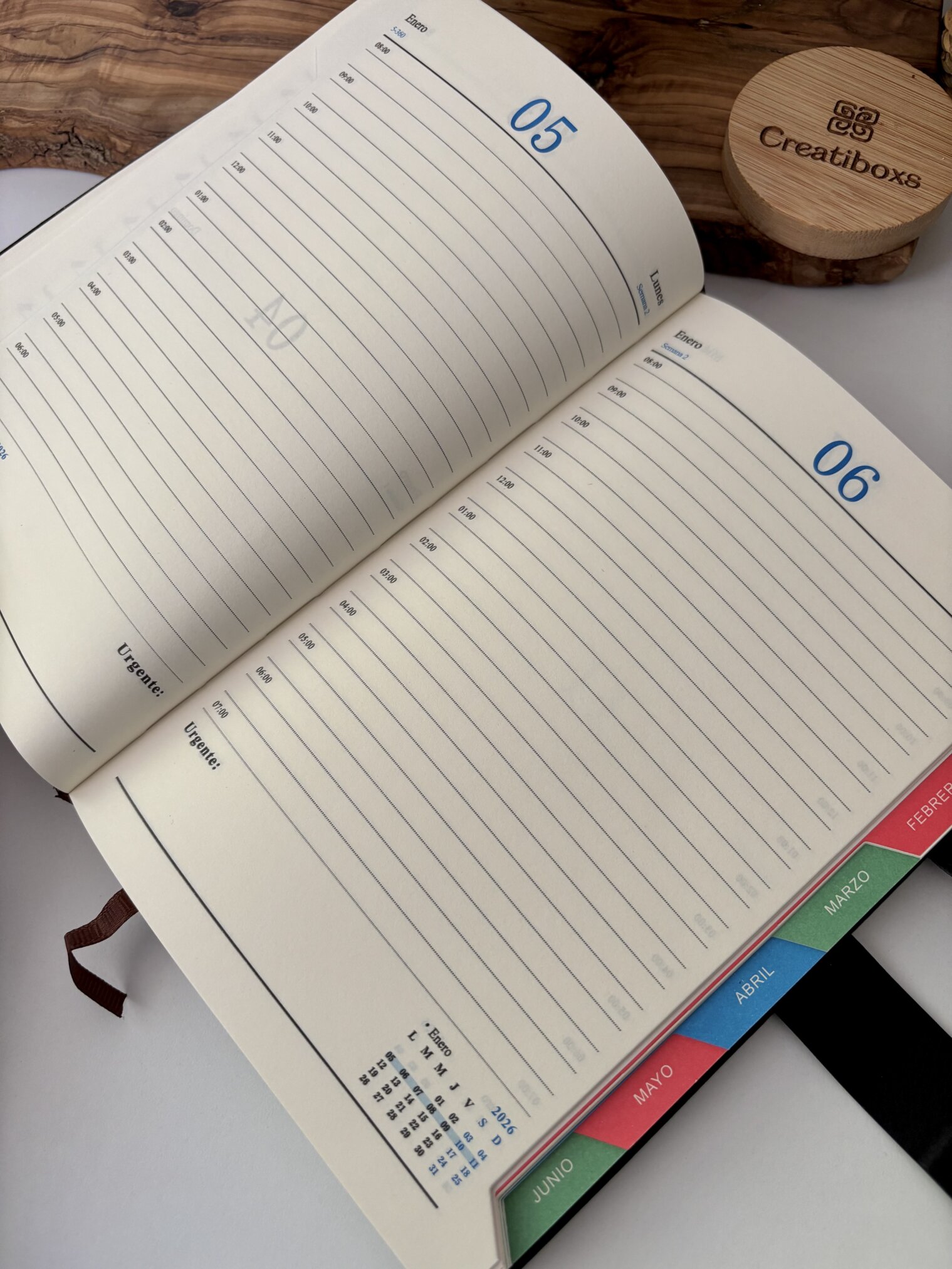 Agenda abierta personalizada A5 con broche magnético rectángulo dorado que muestra las páginas semanales de mayo-junio, pestañas de colores de los meses, e incluye un artículo Creatiboxs de madera.