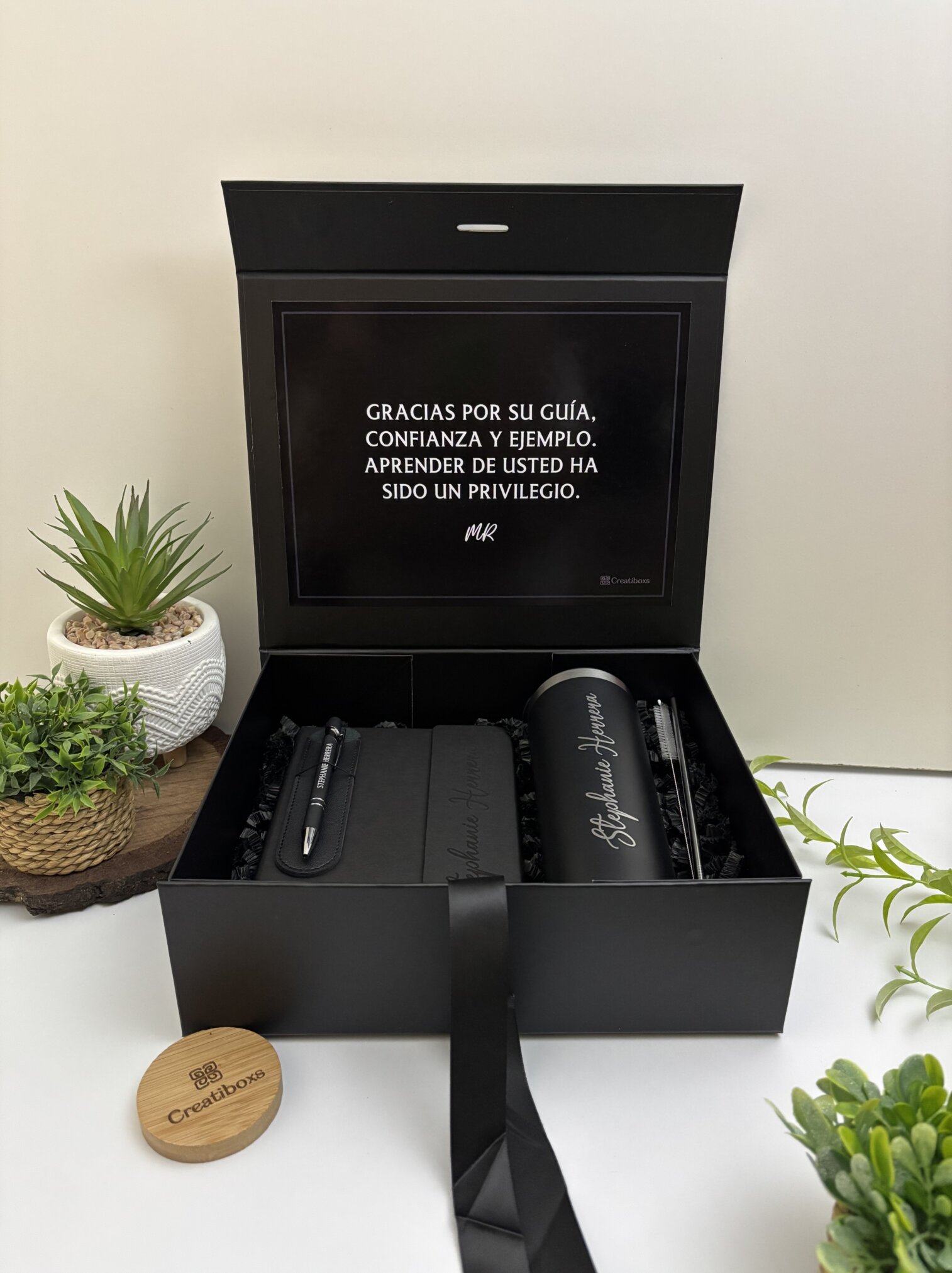 Caja regalo con Kit regalo personalizado en caja: termo delgado 590ml, libreta cierre magnético vertical y bolígrafo, más mensaje de agradecimiento en español, todo decorado entre pequeñas plantas.