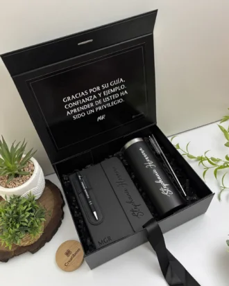 Kit regalo personalizado en caja negra con termo delgado 590ml, libreta cierre magnético vertical y bolígrafo. Incluye mensaje de agradecimiento en español. Perfecto para cualquier ocasión especial.