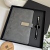 Set libreta con broche magnético plateado y bolígrafo negro en caja, acompañado de una planta y una tapa de madera Creatiboxs.