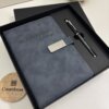 Un Set libreta con broche magnético plateado y bolígrafo negro en caja se coloca junto a un posavasos de madera Creatiboxs para Alejandro.