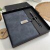 El Set libreta con broche magnético plateado y bolígrafo negro en caja descansa elegantemente sobre el escritorio, personalizado en la portada con Dr. Abel Castill.