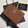 Set personalizado con bolígrafo y libreta con broche plateado, tarjeta de agradecimiento y bolsa de regalo negra, dispuestos sobre una superficie blanca.