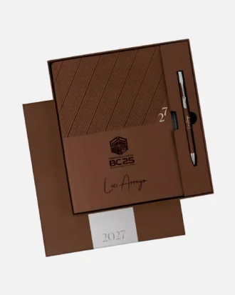 Agenda semanal clásica personalizada de 2027 en color marrón, con bolígrafo, presentada en caja y con el logotipo BC25 y la firma en la portada.