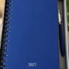 Agenda diaria 2027 de curpiel azul con encuadernación de arillo y bolígrafo metálico en caja individual.